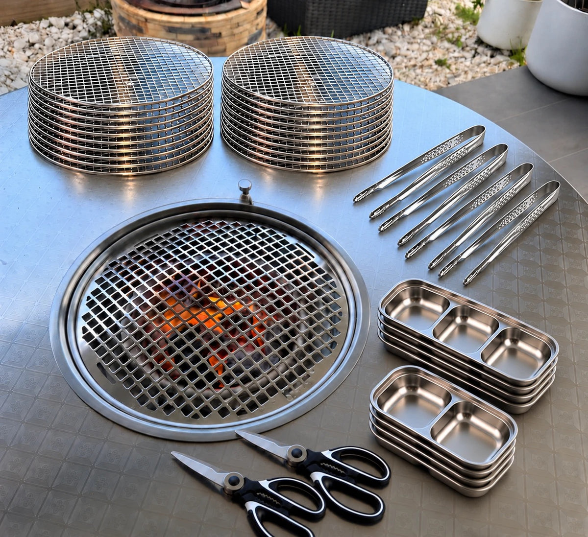 Entertainer Kit laid out on a KBBQ table outdoors: 20 disposable grill meshes, 4 tongs, 4 three-grid and 4 two-grid sauce trays, 2 meat scissors