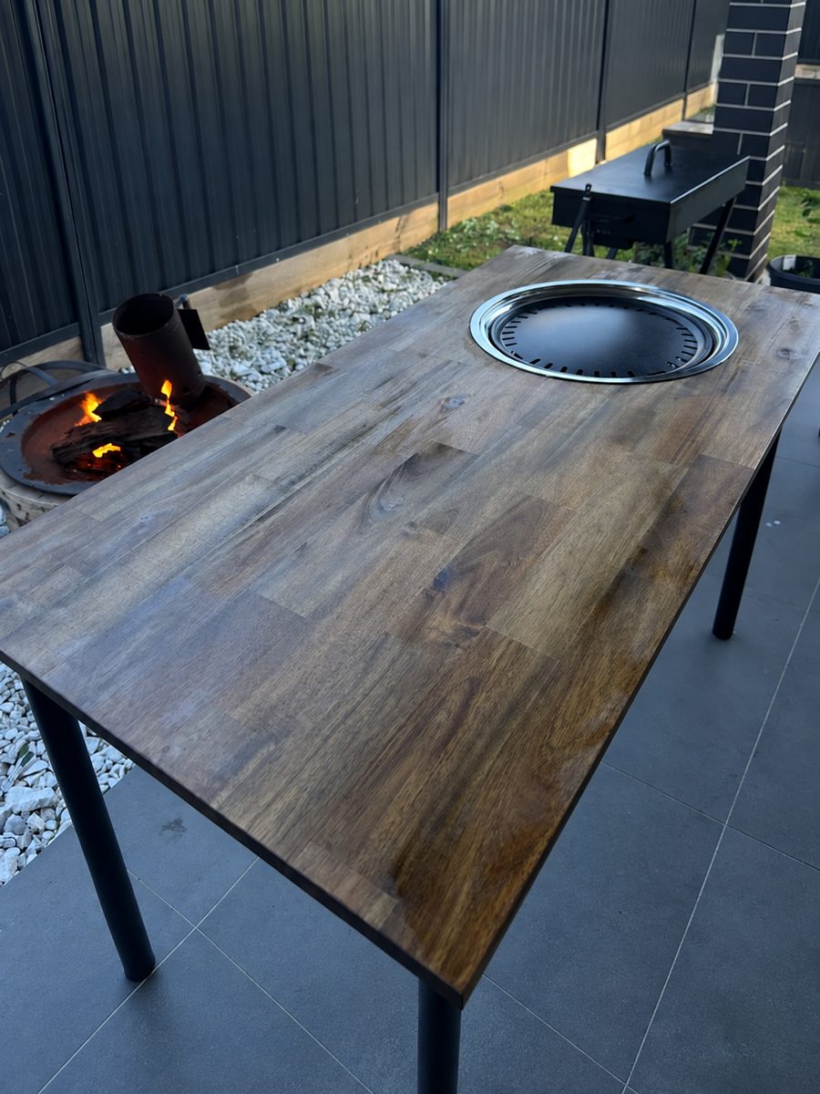 The first KBBQ PLUG table: a timber top with a grill insert, in a backyard
